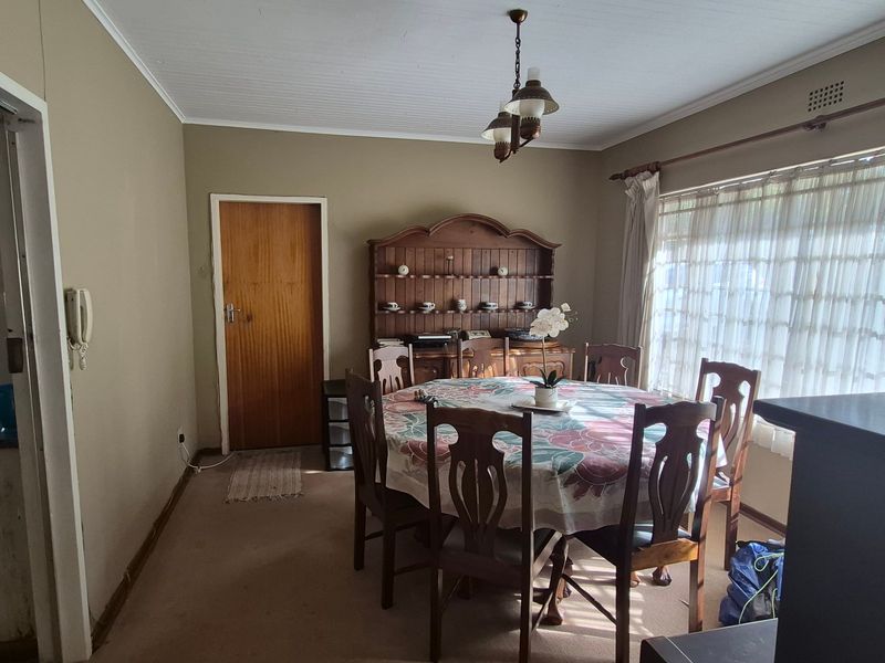 A traditional dining room featuring carpeted flooring, a timber door, and a classic ceiling light fixture, offering a dated but functional space.
