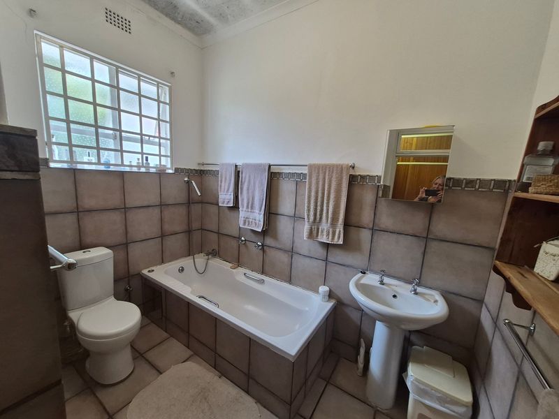 A functional bathroom featuring a pedestal basin, built-in bathtub, and tiled finishes. The space is well-lit with natural light from the window.