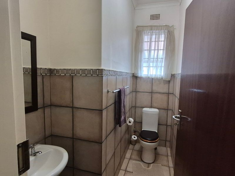 A functional guest bathroom featuring neutral ceramic wall and floor tiles, a pedestal basin, and a standard toilet.