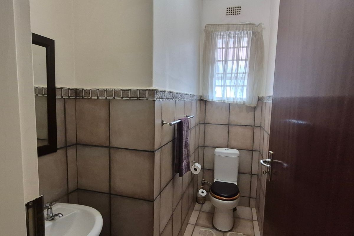 A functional guest bathroom featuring neutral ceramic wall and floor tiles, a pedestal basin, and a standard toilet.