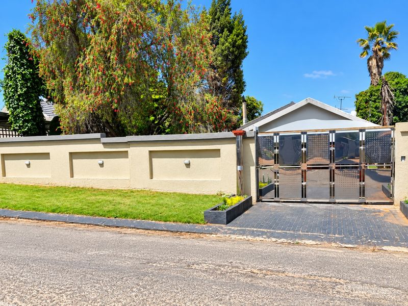 Front view of the property featuring a secure stainless steel driveway gate, perimeter wall with integrated lighting, and a paved driveway.