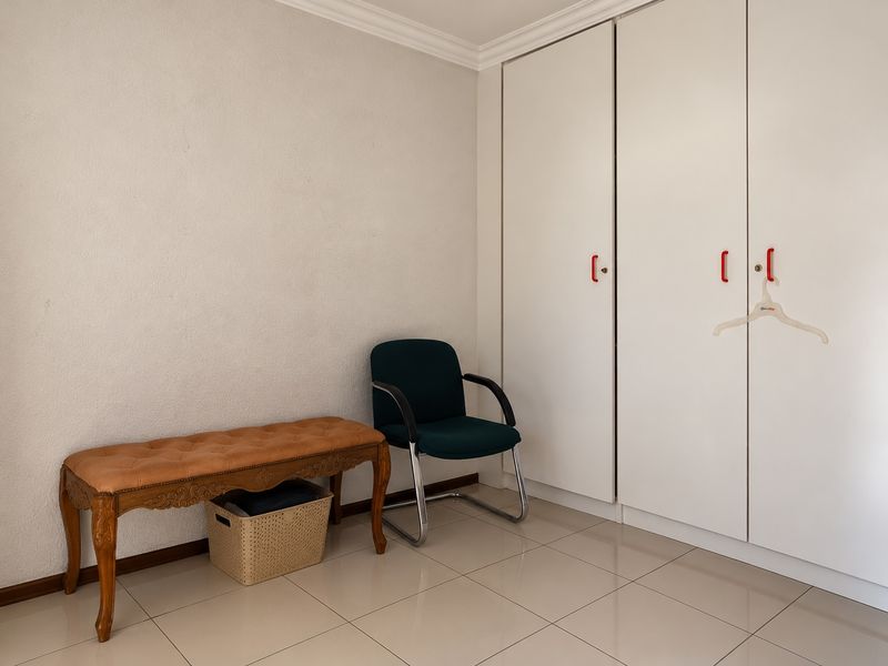 A bedroom featuring neutral tiled flooring, white walls with decorative cornicing, and ample built-in cupboard storage.