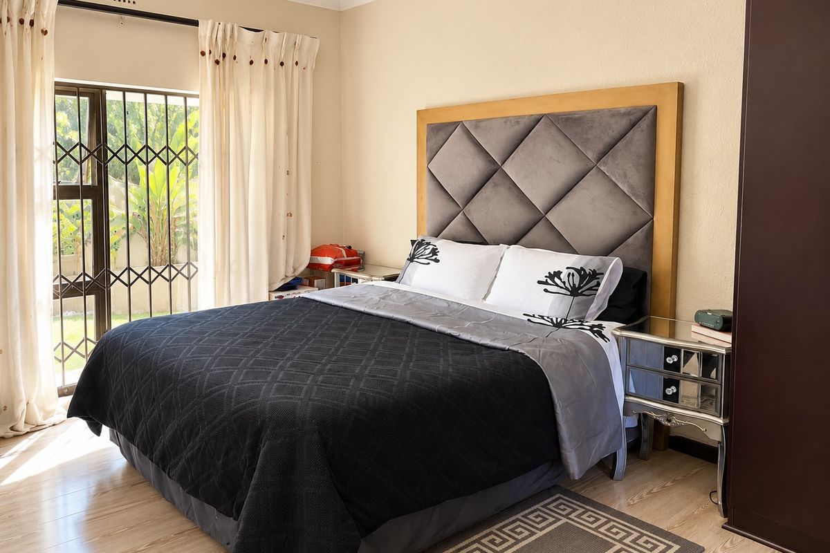 A well-maintained bedroom featuring laminate flooring, a large upholstered headboard, and a sliding door with a security gate leading to the garden.