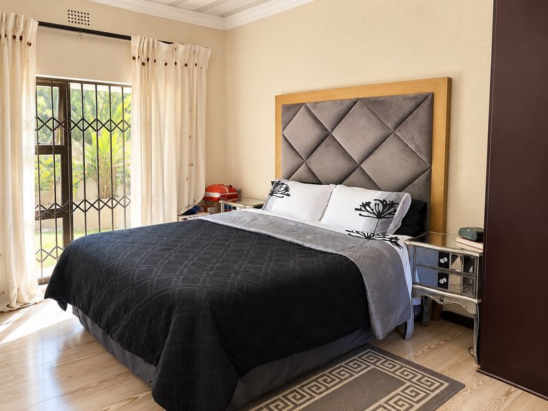 A well-maintained bedroom featuring laminate flooring, a large upholstered headboard, and a sliding door with a security gate leading to the garden.