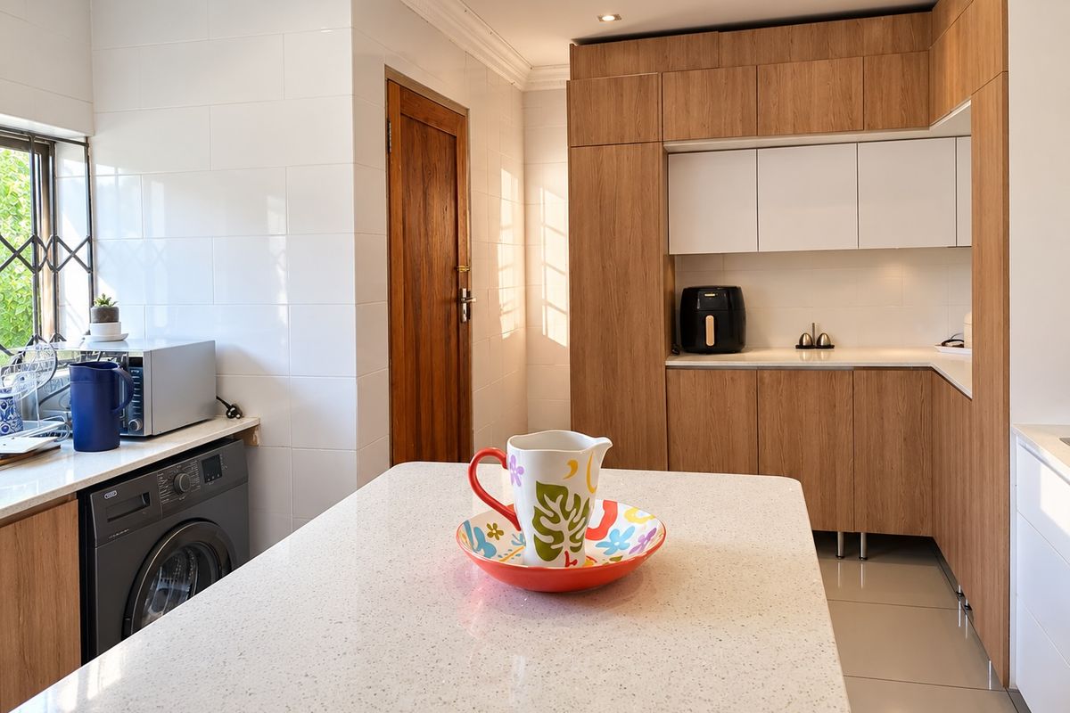 Modern kitchen featuring wood-grain cabinetry, quartz countertops, integrated laundry appliances, and clean tiled finishes with ample natural light.