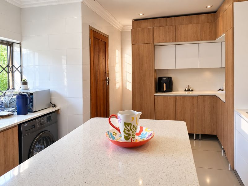 Modern kitchen featuring wood-grain cabinetry, quartz countertops, integrated laundry appliances, and clean tiled finishes with ample natural light.