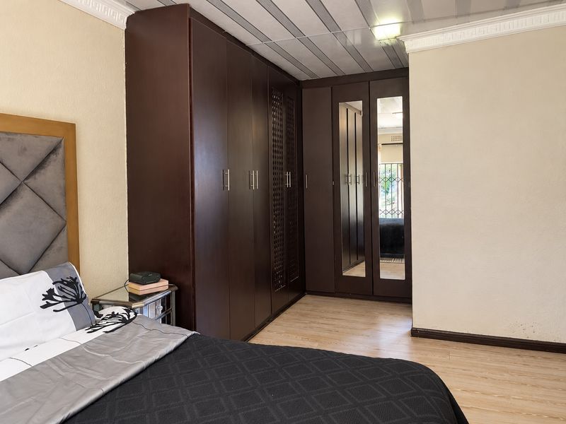 A bedroom featuring extensive dark wood built-in cupboards with mirrored panels, laminate flooring, and decorative ceiling cornicing.