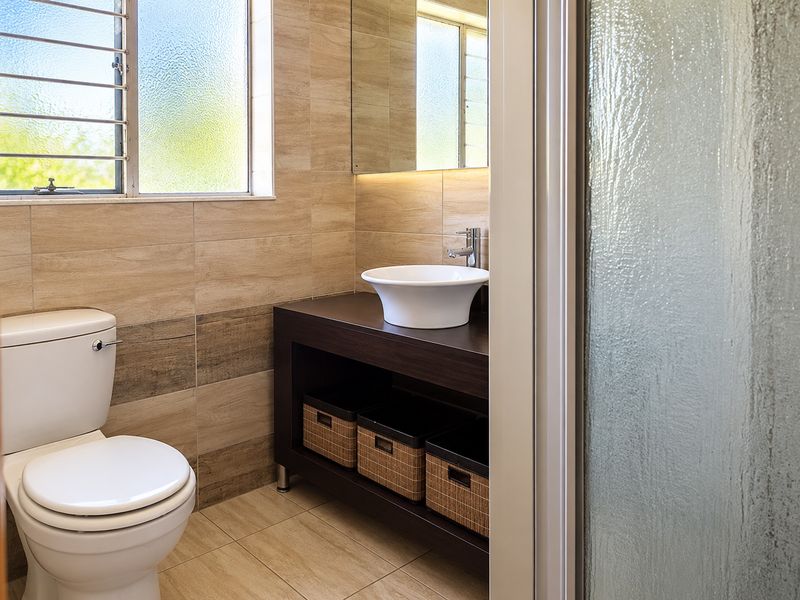 A modern bathroom featuring a vessel sink on a dark vanity cabinet, tiled walls, and a frosted glass window with security bars.