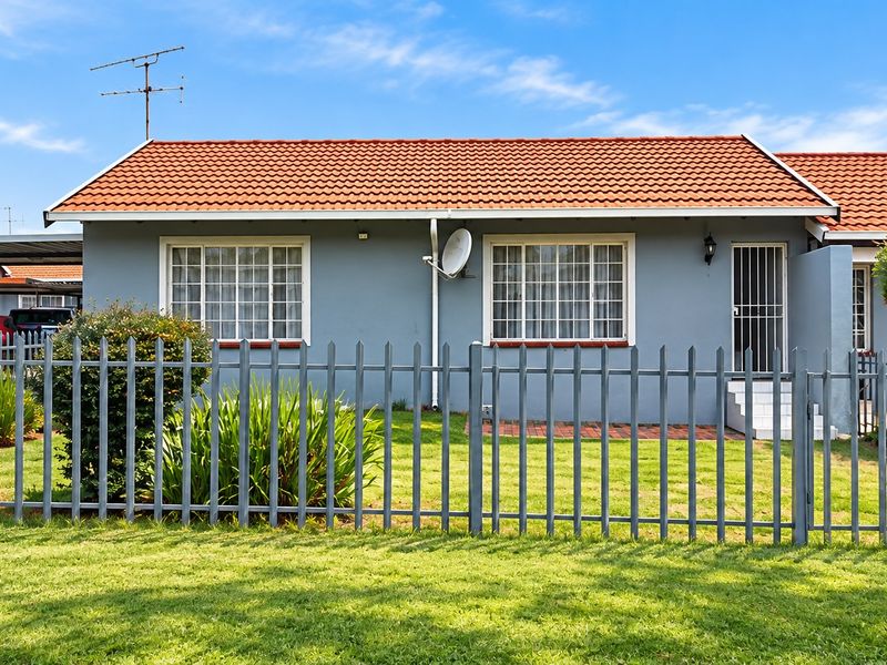 Front view of a single-story residential home featuring a terracotta tiled roof, grey exterior walls, and secure steel palisade fencing with a front garden.