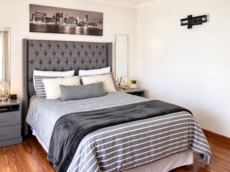 A well-maintained bedroom featuring warm-toned laminate flooring and a wall-mounted television bracket, offering a clean and functional living space.