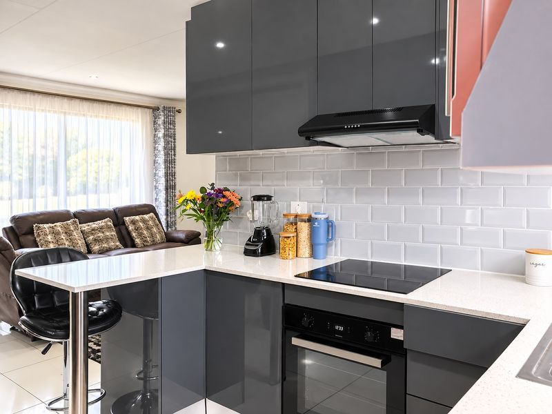 Modern open-plan kitchen featuring sleek grey cabinetry, subway tile backsplash, quartz countertops, and integrated appliances, seamlessly flowing into the adjacent living area.