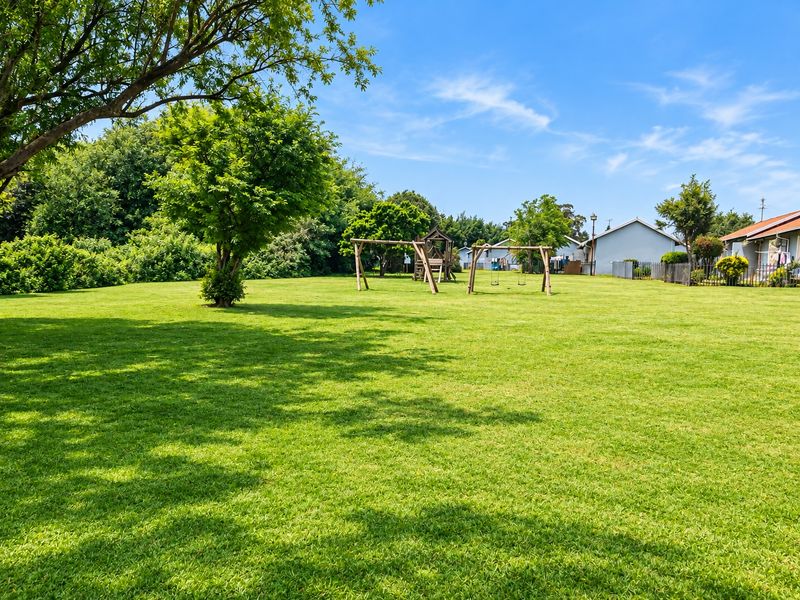 A spacious, well-maintained green garden area featuring mature trees and open lawn space, providing a pleasant outdoor environment.