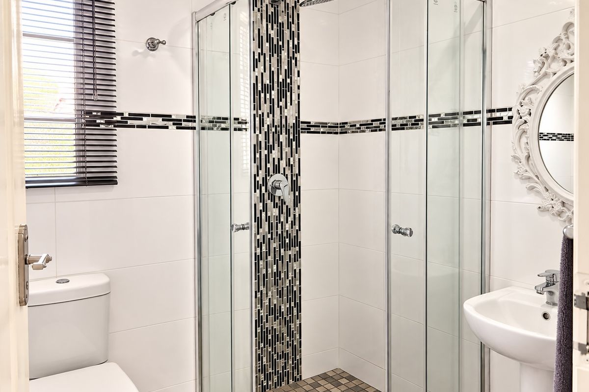 Modern bathroom featuring a glass shower enclosure with mosaic tile accents, a pedestal basin, and a clean white tiled finish.
