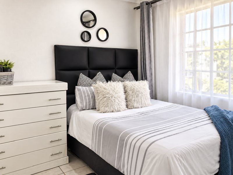 A well-lit bedroom featuring tiled flooring and a large grid-pattern window, providing a bright and comfortable living space.