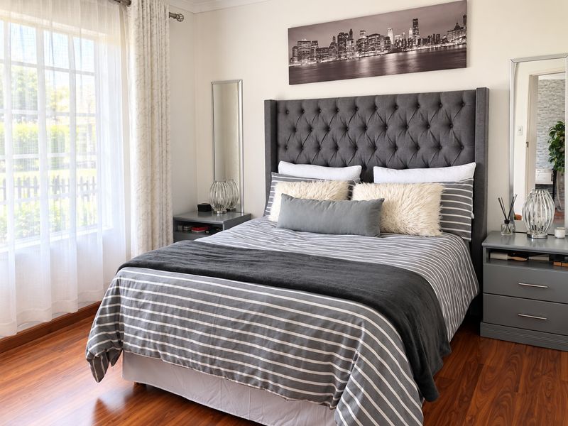 A well-maintained bedroom featuring warm-toned laminate flooring and a large window that allows for ample natural light.