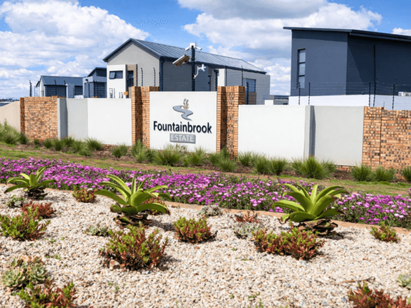 The entrance to Fountainbrook Estate featuring a modern brick and rendered boundary wall, security infrastructure, and well-maintained landscaped garden beds.