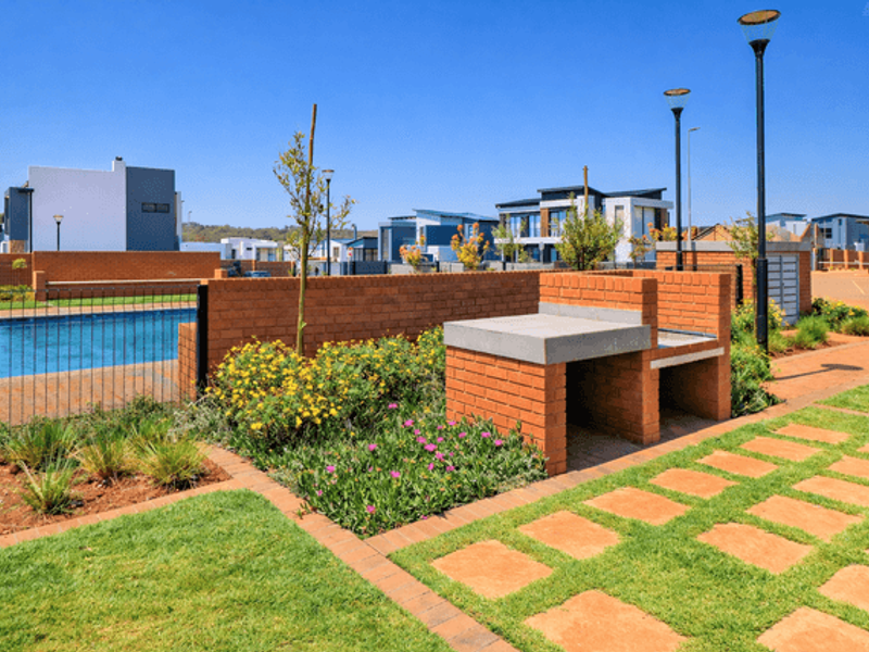 Communal pool area featuring a built-in brick braai, paved walkways, and landscaped garden beds within a secure residential estate.