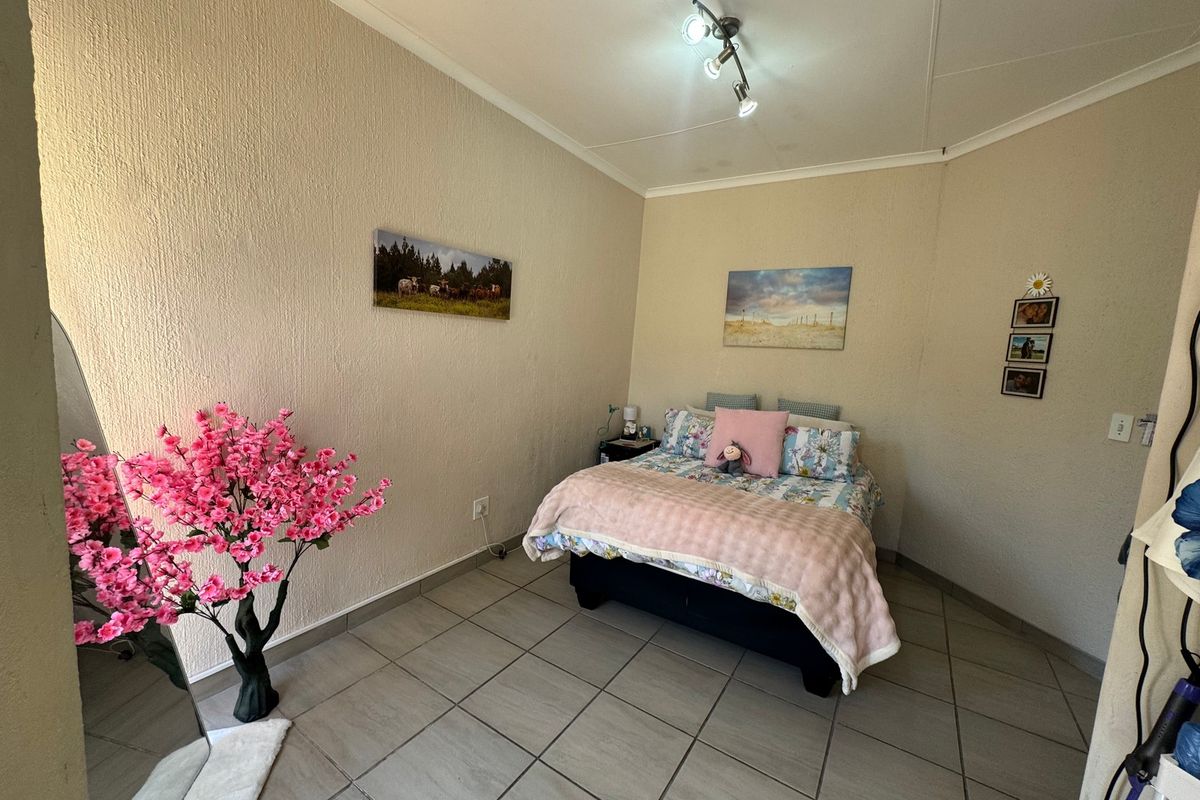A bedroom featuring neutral textured walls and tiled flooring, illuminated by a modern ceiling-mounted spotlight fixture.