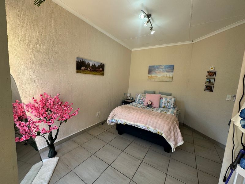 A bedroom featuring neutral textured walls and tiled flooring, illuminated by a modern ceiling-mounted spotlight fixture.