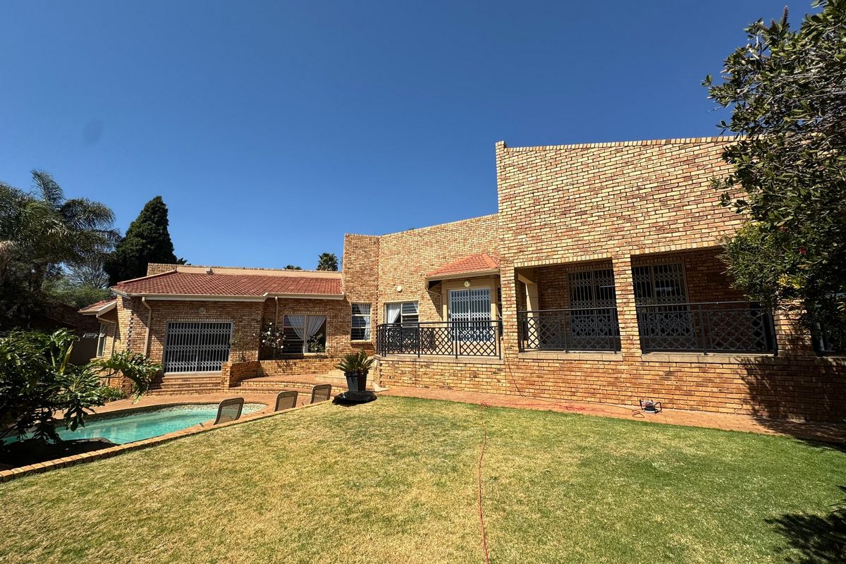 Rear view of a face brick house featuring a swimming pool, paved patio area, and secure metal railings.