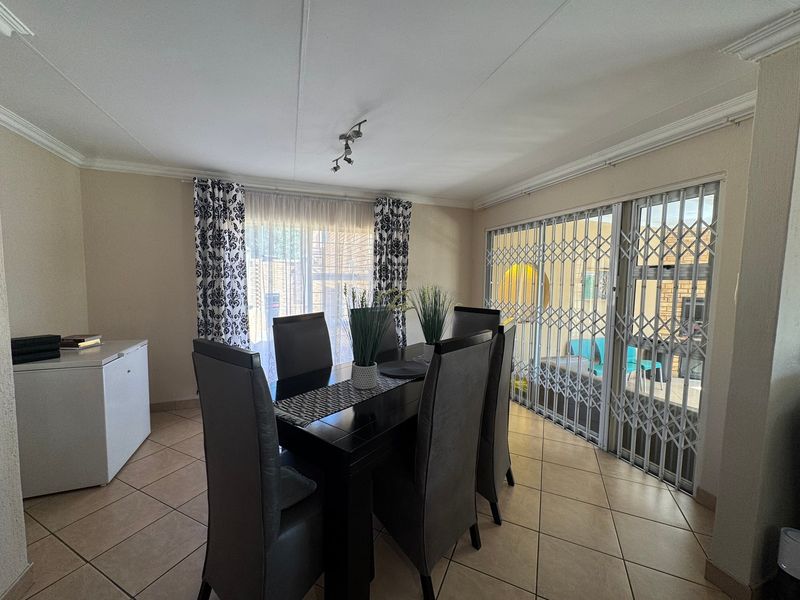A dining room featuring tiled flooring, ceiling cornice, and sliding glass doors with security gates leading to an outdoor area.