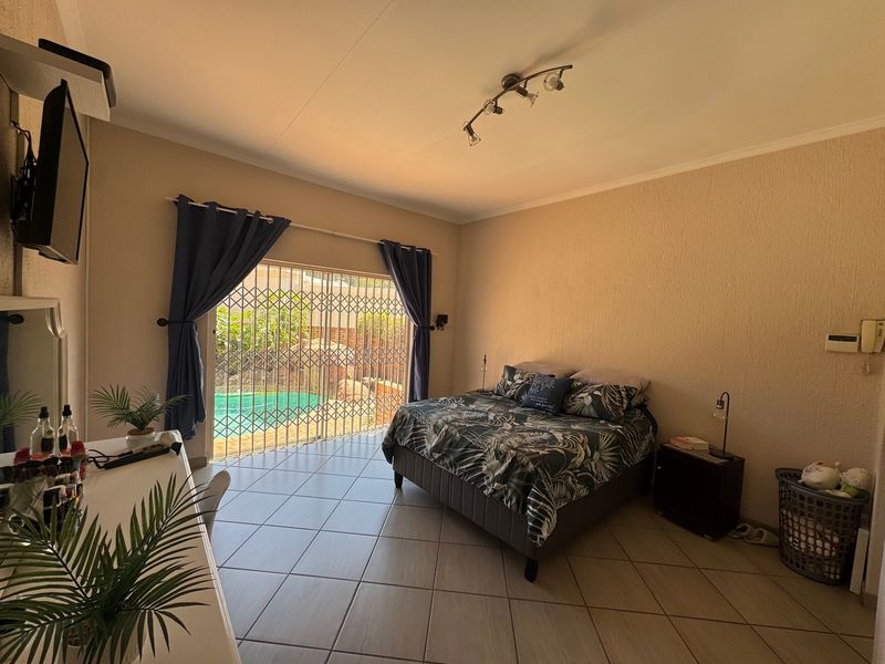 Spacious bedroom featuring tiled flooring and a sliding glass door with security gate, providing direct access to the outdoor pool area.