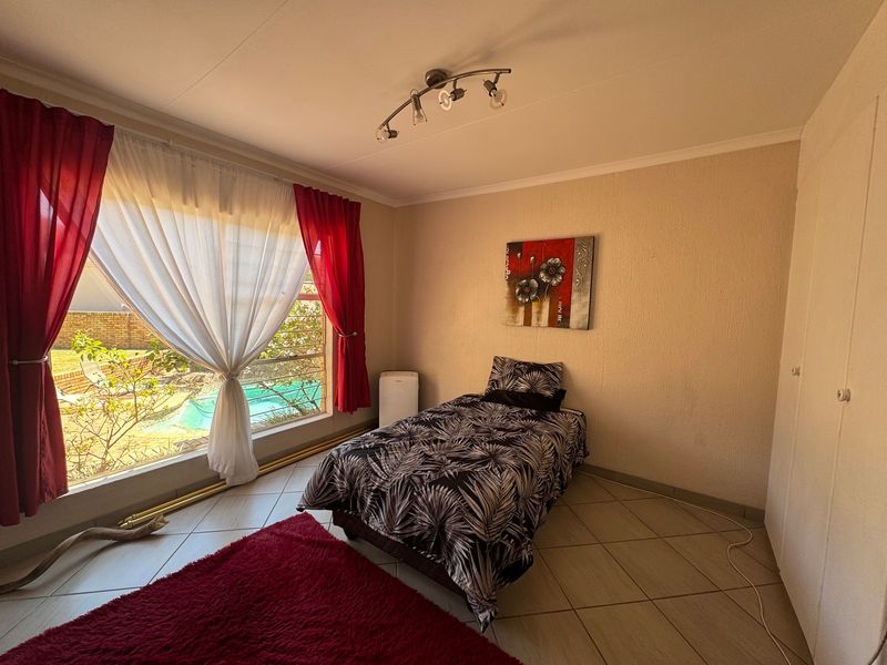 A bedroom featuring tiled flooring, a built-in cupboard, and a large window providing natural light and a view of the outdoor pool area.