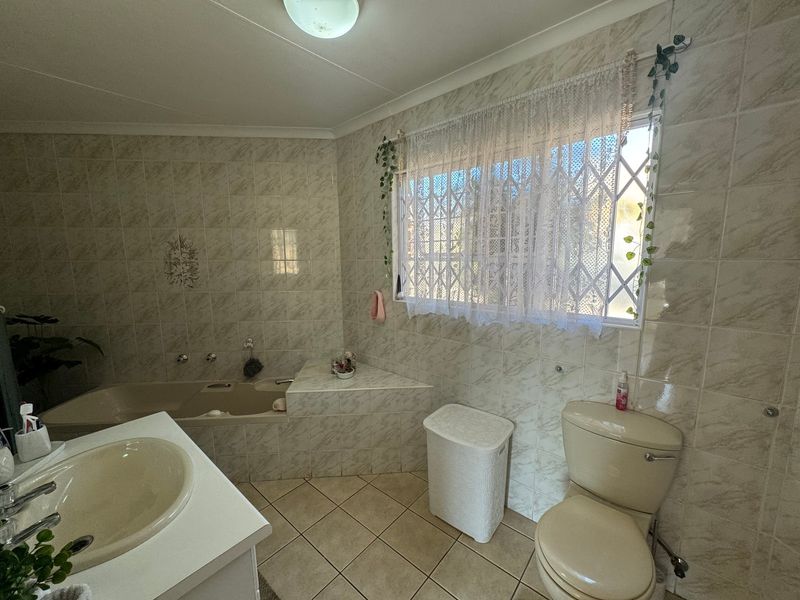 A functional bathroom featuring a built-in bathtub, vanity basin, and toilet, finished with neutral ceramic wall and floor tiles.