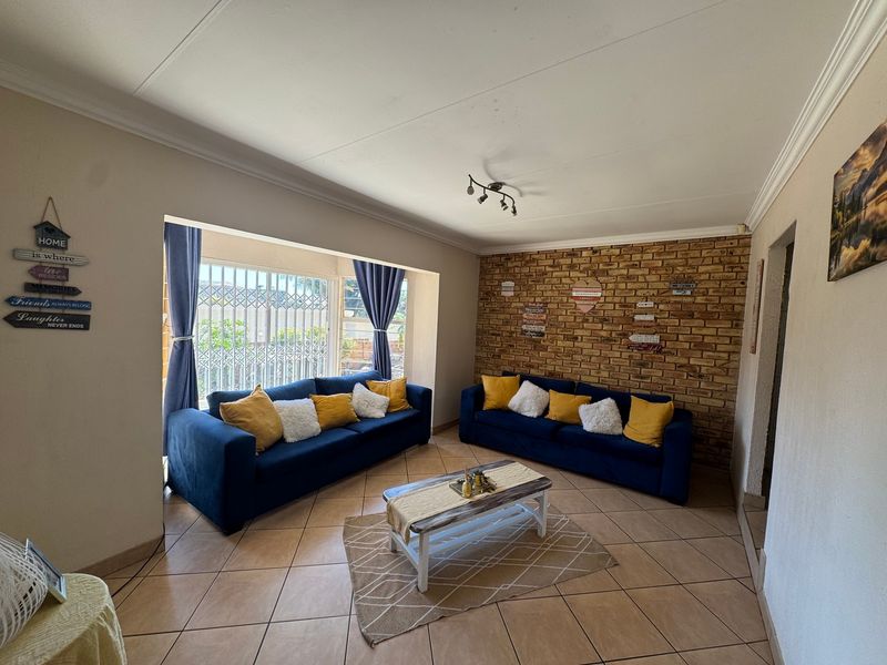 A comfortable living room featuring an exposed brick accent wall, ceramic tiled flooring, and large windows with integrated security gates.