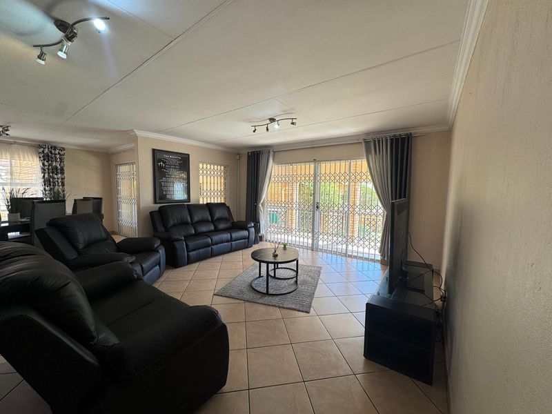 Spacious living room featuring tiled flooring, coved ceilings, and a sliding glass door with security gate providing access to the outdoor area.