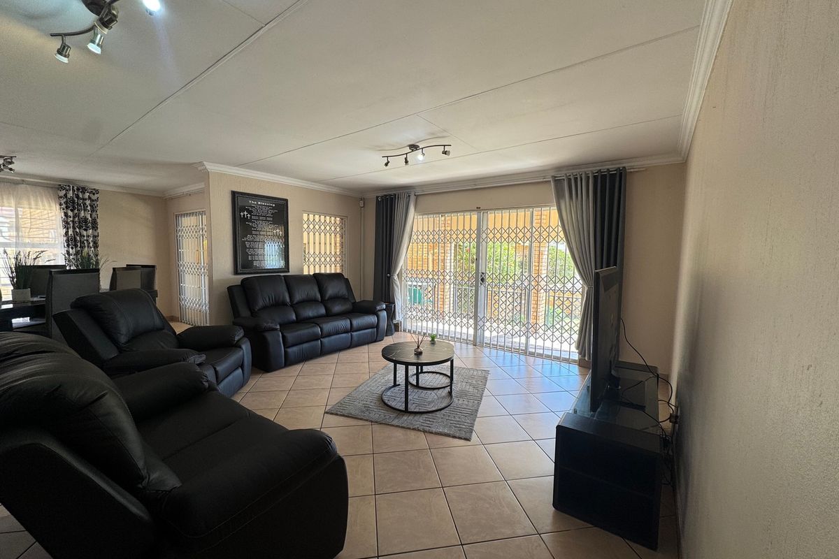 Spacious living room featuring tiled flooring, coved ceilings, and a sliding glass door with security gate providing access to the outdoor area.