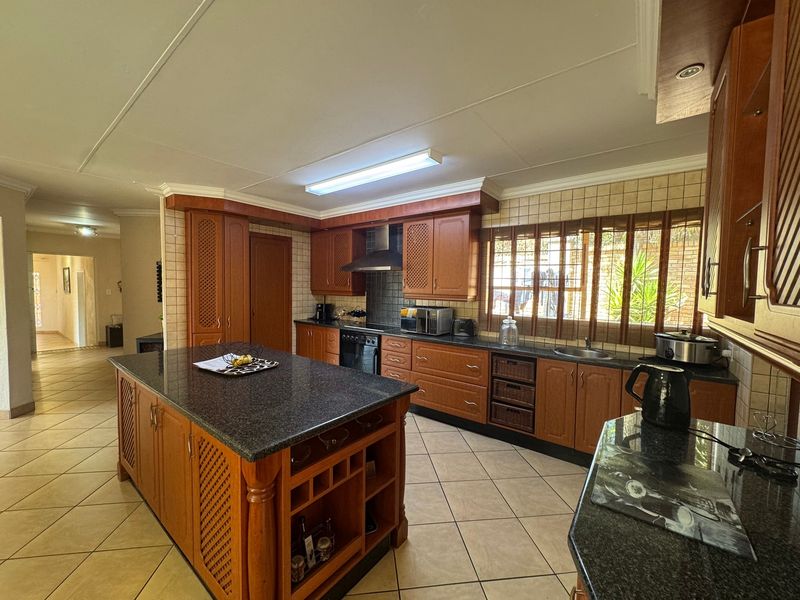 Spacious kitchen featuring a central island, granite countertops, wooden cabinetry, and tiled flooring, offering a functional layout with ample storage space.