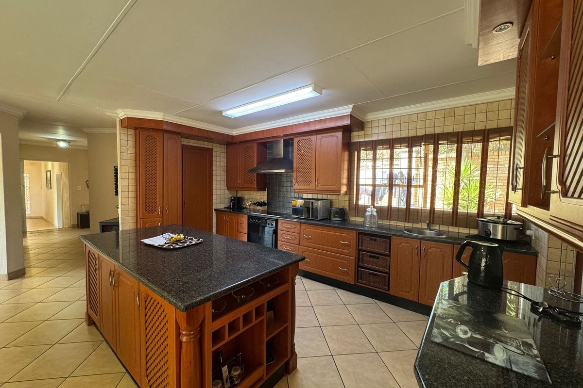 Spacious kitchen featuring a central island, granite countertops, wooden cabinetry, and tiled flooring, offering a functional layout with ample storage space.