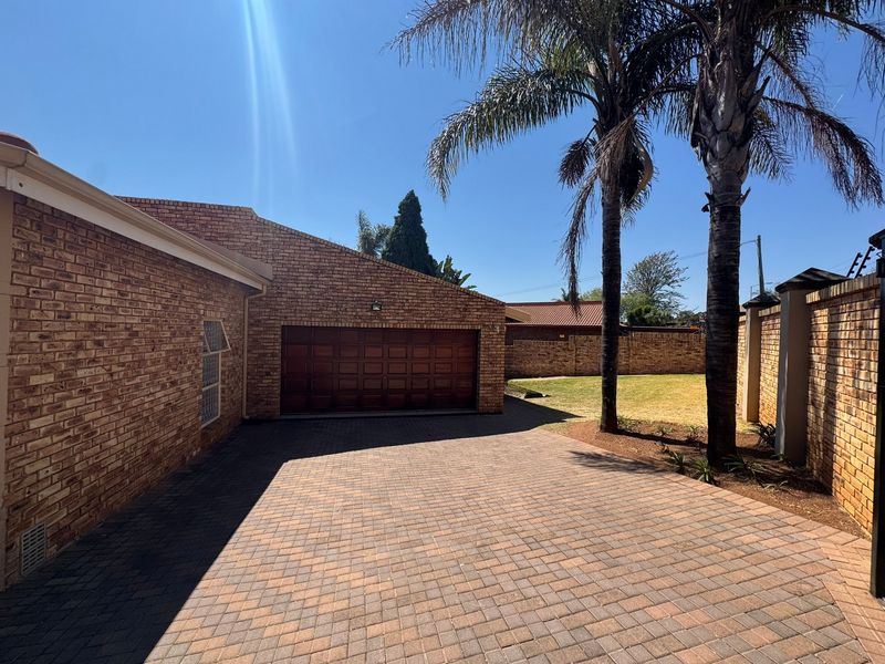 A well-maintained front exterior featuring a paved driveway, face-brick facade, and a secure sectional garage door with established palm trees.