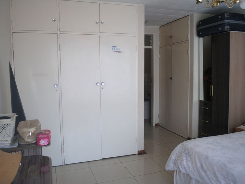 A bedroom featuring extensive built-in cupboard storage and neutral tiled flooring, providing a functional layout with direct access to an adjoining space.