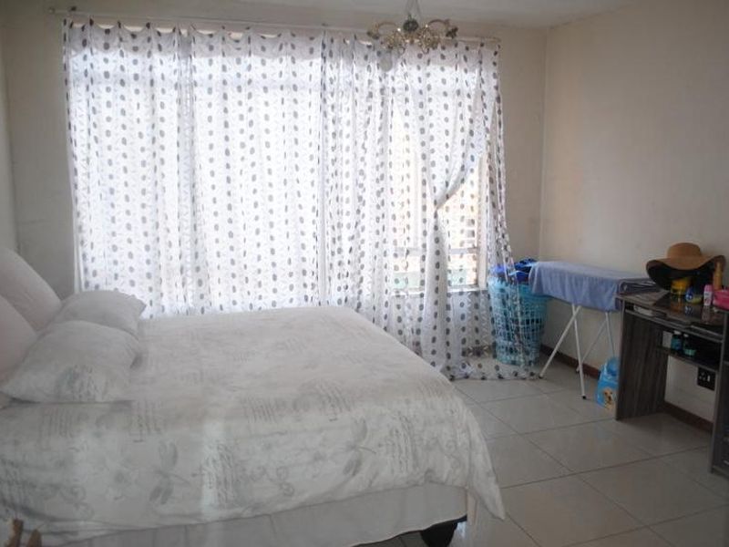 A bedroom featuring tiled flooring and a large window with curtains, providing natural light to the space.