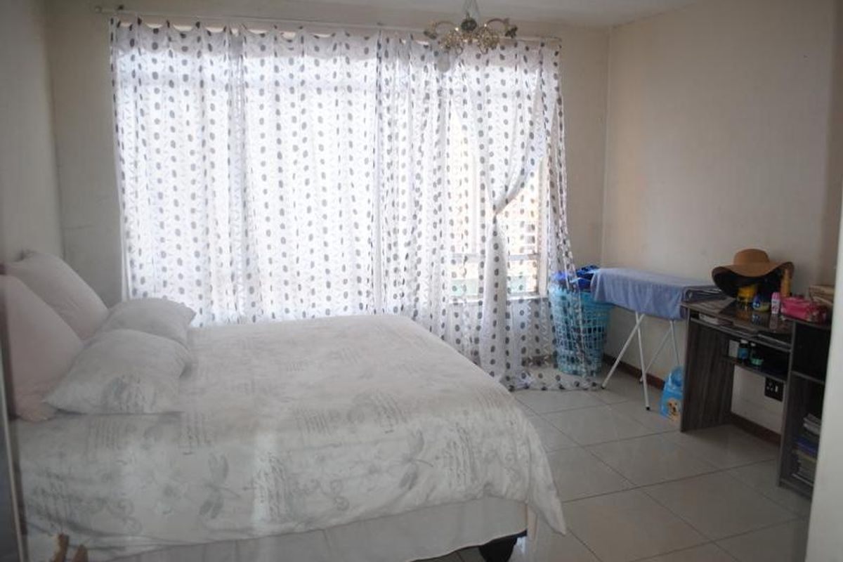 A bedroom featuring tiled flooring and a large window with curtains, providing natural light to the space.