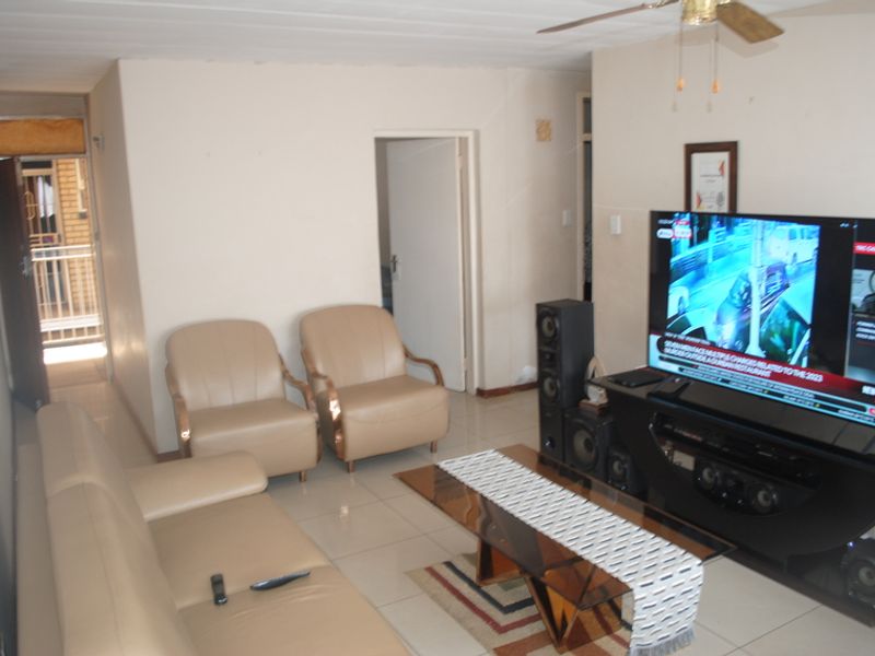 A living room area featuring tiled flooring and a ceiling fan, with visible signs of wear on the walls and ceiling.