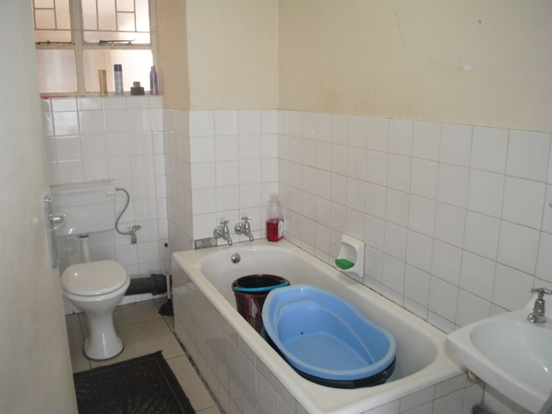A functional bathroom featuring a standard bathtub, toilet, and washbasin with white wall tiling and visible signs of wear on the wall surfaces.
