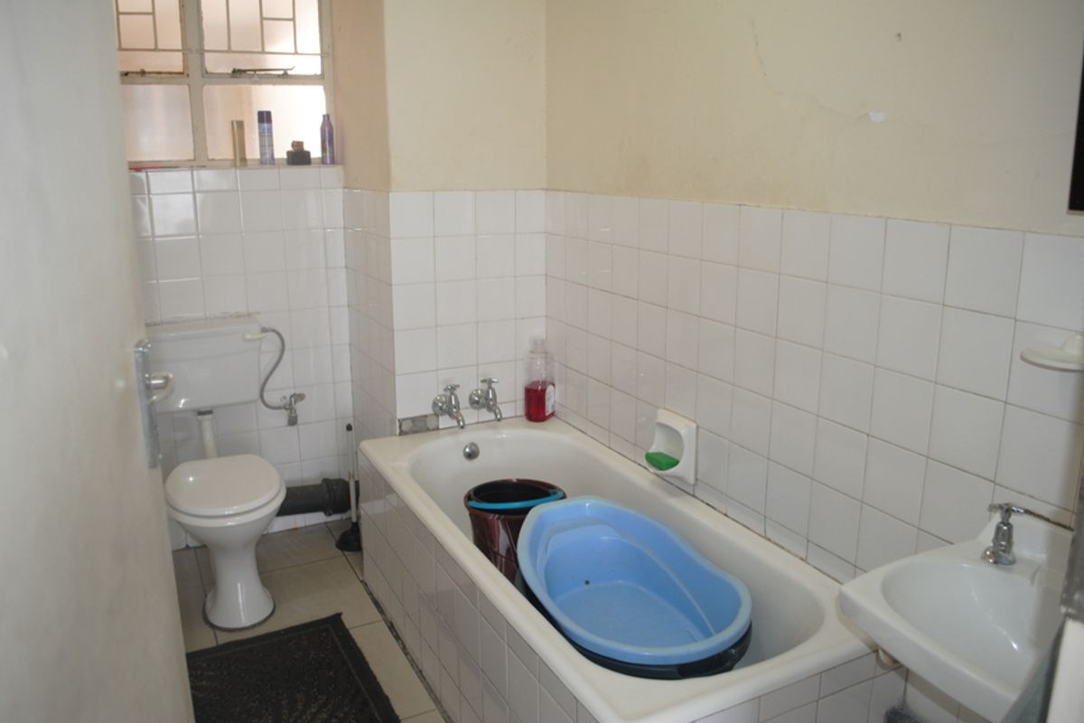A functional bathroom featuring a standard bathtub, toilet, and washbasin with white wall tiling and visible signs of wear on the wall surfaces.