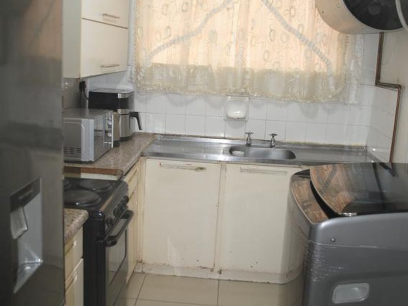 Compact kitchen featuring tiled flooring, built-in cabinetry, a stainless steel sink, and a wall-mounted geyser, requiring cosmetic updates to modernize the space.
