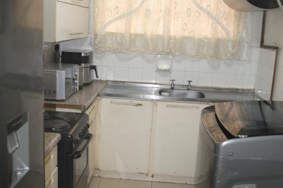 Compact kitchen featuring tiled flooring, built-in cabinetry, a stainless steel sink, and a wall-mounted geyser, requiring cosmetic updates to modernize the space.