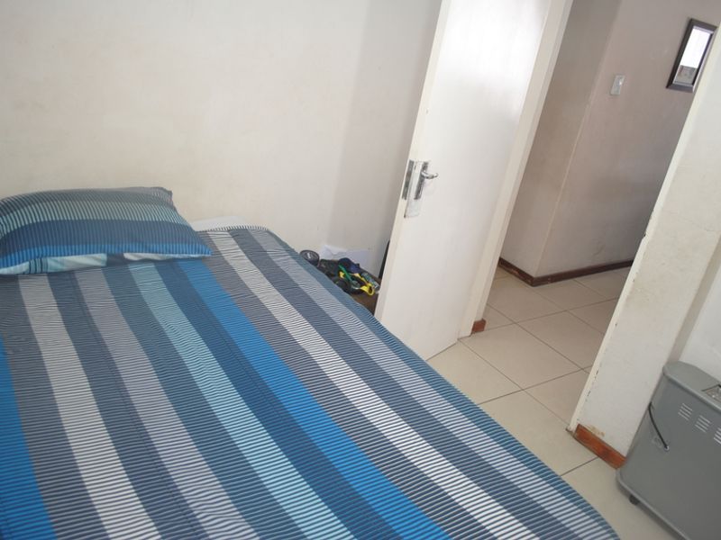 A compact bedroom featuring tiled flooring and an internal door leading to a hallway area.