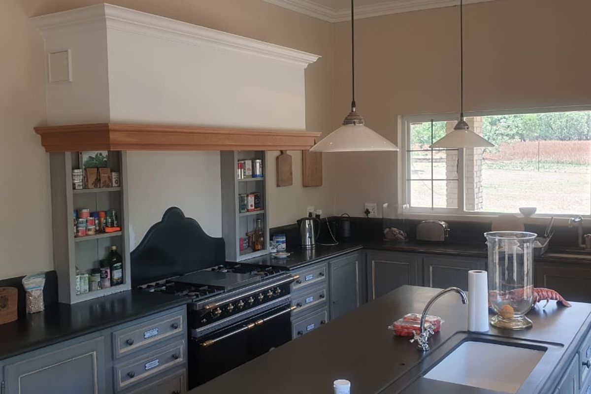 A well-appointed farmhouse kitchen featuring dark cabinetry, a central island with a sink, stone countertops, and a professional-style range cooker with an extractor hood.