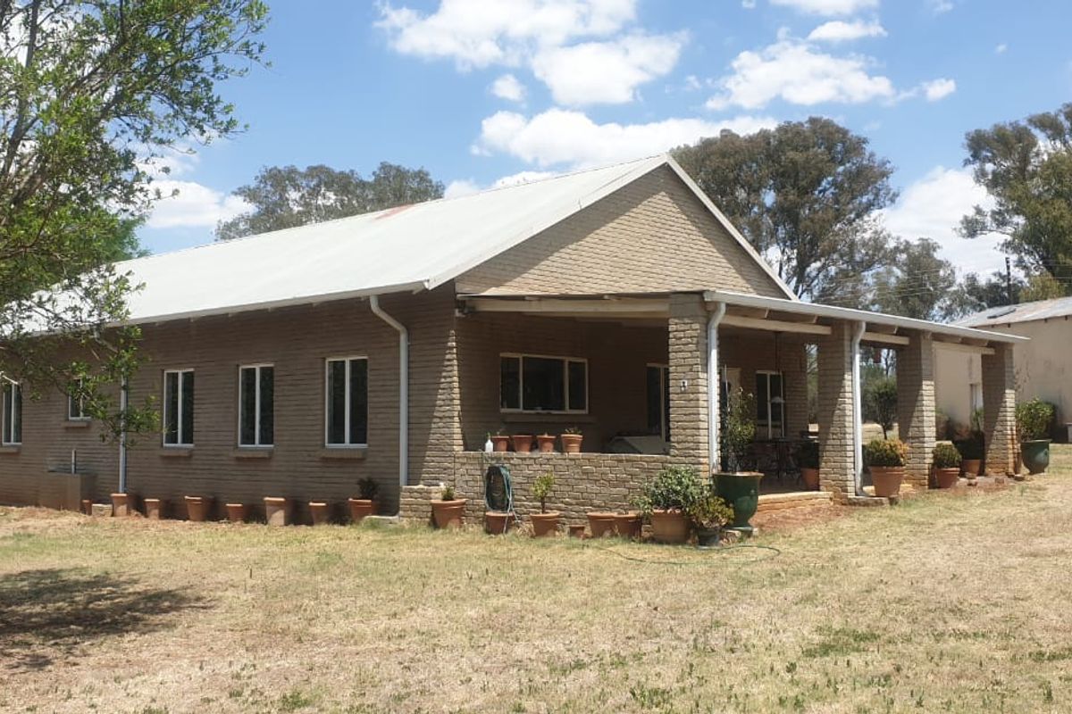 Rear view of a farm-style dwelling featuring a corrugated metal roof, brick exterior, and a spacious covered patio area.