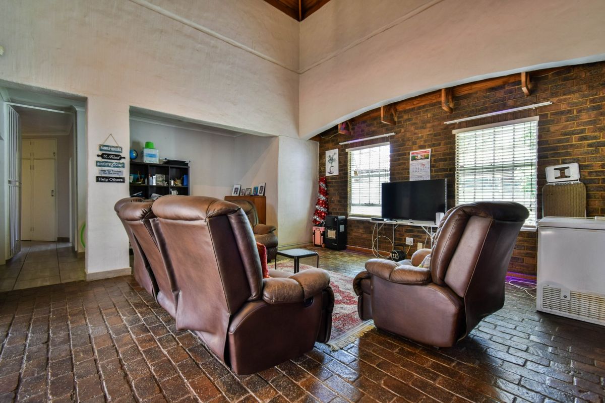 Spacious living room featuring high vaulted timber ceilings, exposed brick walls, and rustic brick flooring, offering a warm and character-filled atmosphere.