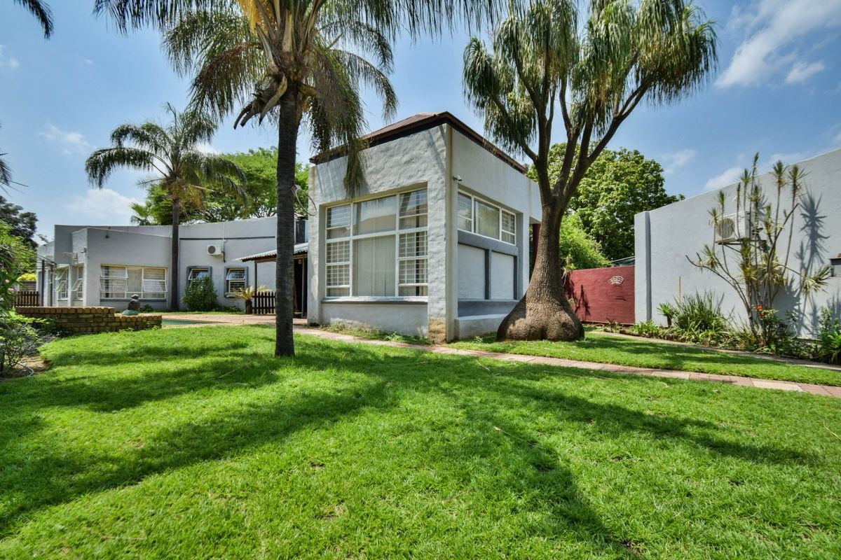 Rear view of the property featuring a landscaped garden, swimming pool, paved pathways, and established trees against the building facade.
