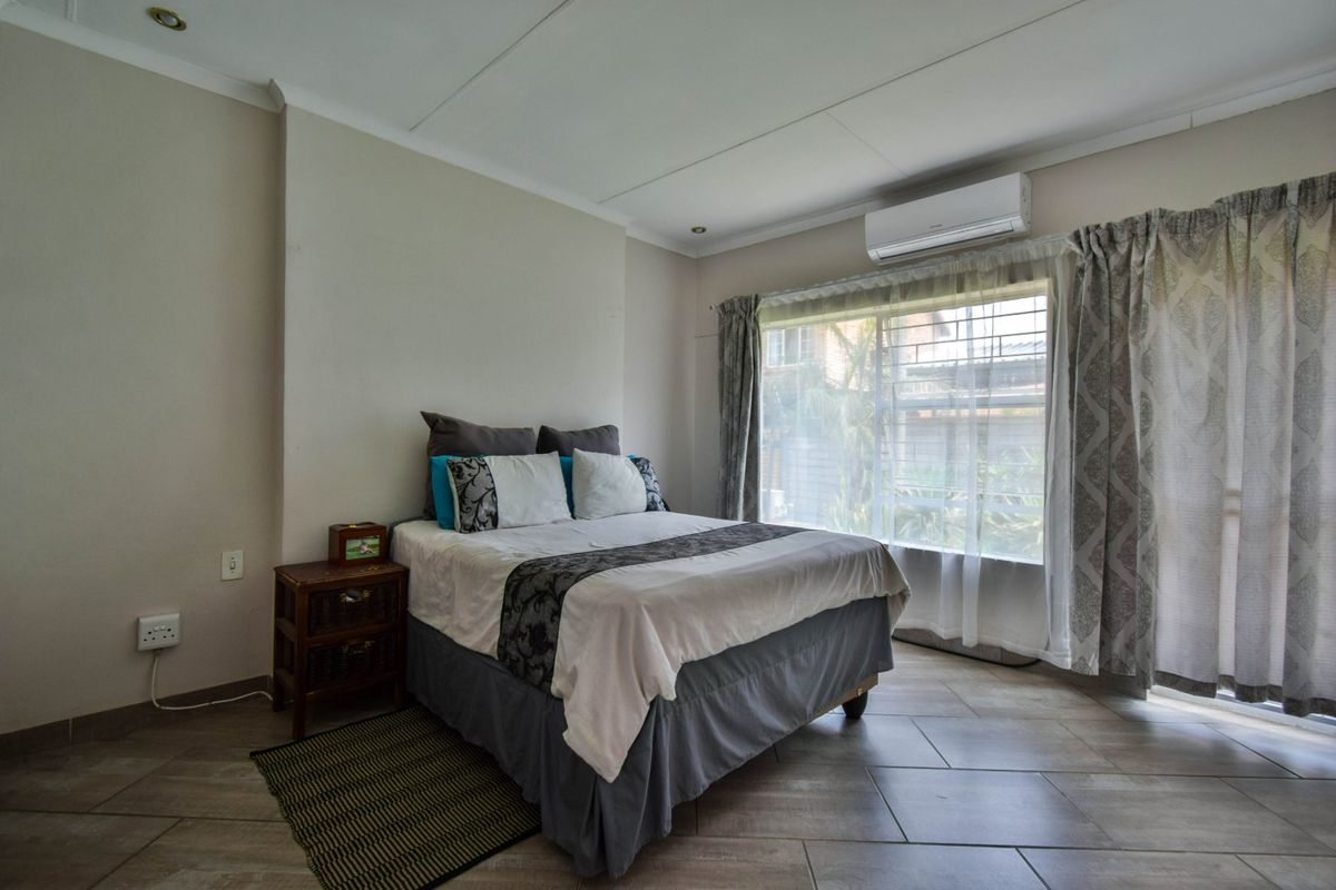 A well-maintained bedroom featuring tiled flooring, a wall-mounted split-system air conditioner, and large windows with security bars.