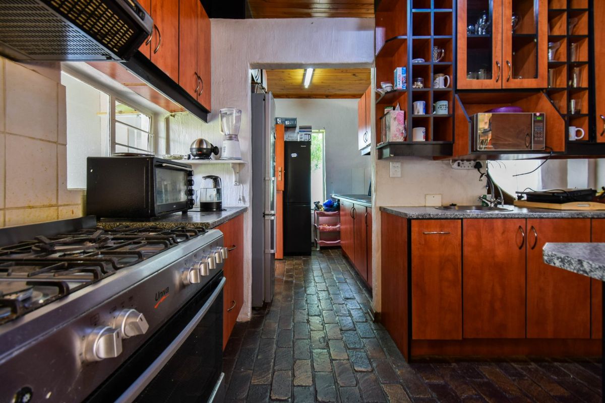 A functional kitchen featuring wooden cabinetry, granite countertops, a gas stove with extractor, and distinctive brick flooring leading to a secondary utility area.