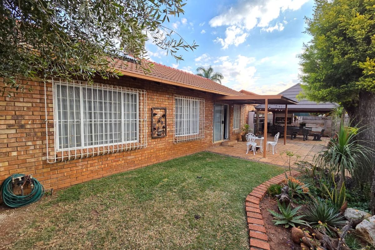 Rear view of the townhouse featuring a face-brick facade, a paved covered patio area, and a well-maintained garden with established landscaping.